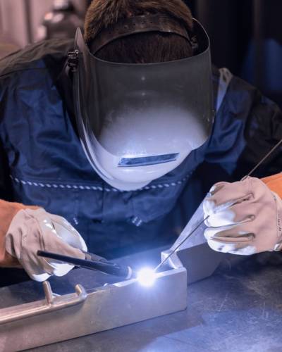 Spot welder joins steel beams. A closeup and side profile of a metalworker using a gas metal arc welding machine to join two pieces of steel. Skilled worker